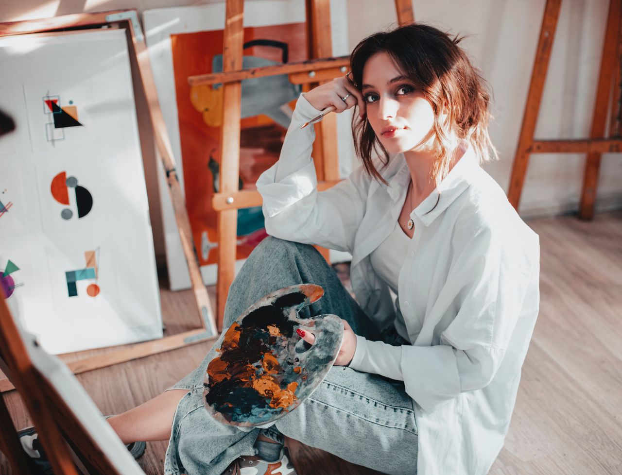 about-us-01 Portrait of a woman artist in a Baku studio, surrounded by abstract paintings and easels.