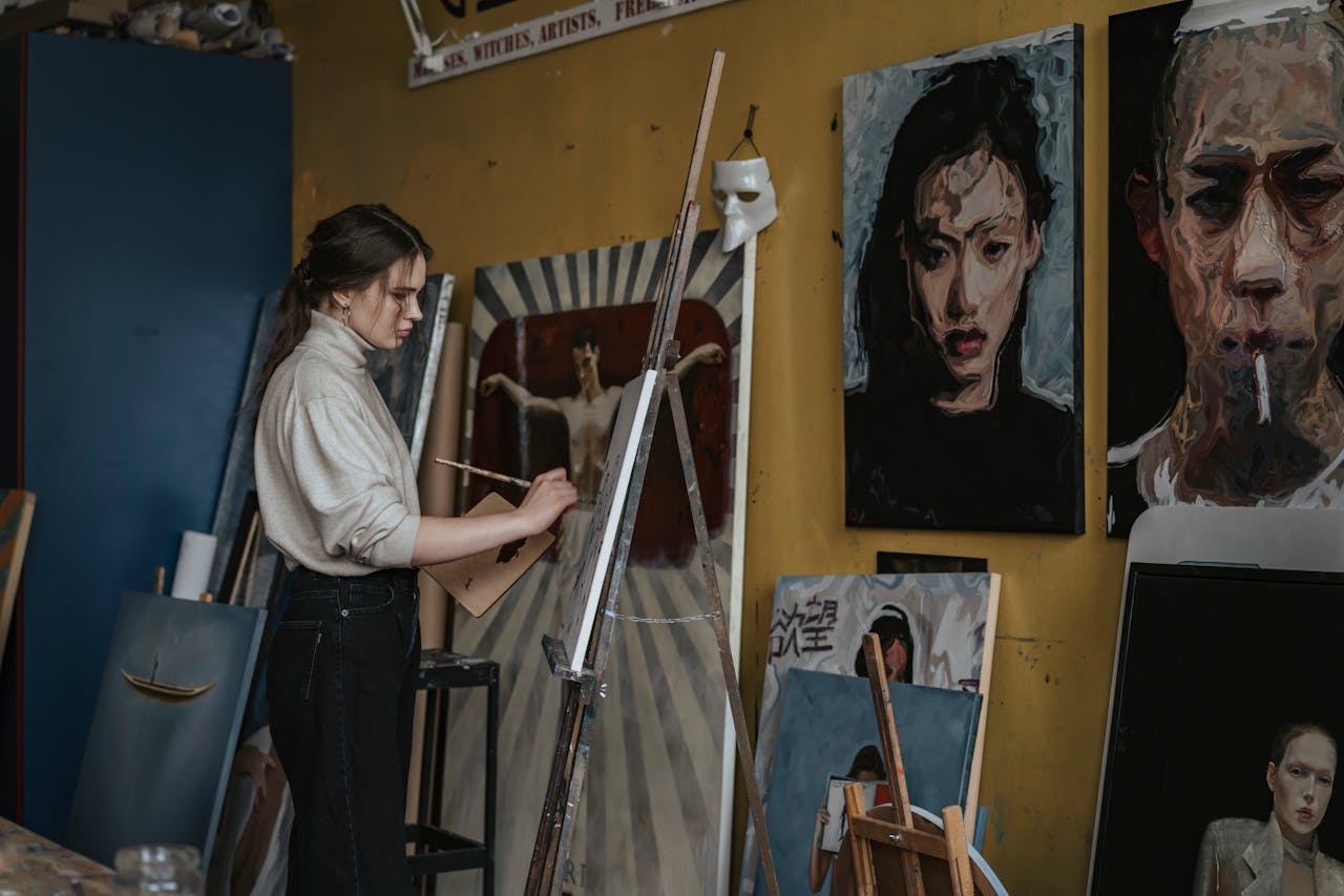 services-02 Artist creates paintings in a studio surrounded by expressive portrait artworks.